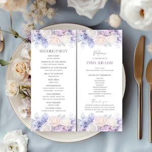 May include: A wedding program with floral accents in shades of purple, lavender, and white, displayed on a plate with gold cutlery. The program includes the wedding party details and ceremony order, with the names of the bride and groom prominently featured.