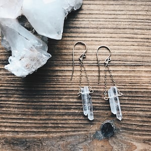 May include: A pair of silver earrings with clear crystal teardrop pendants hanging from delicate gold chains.