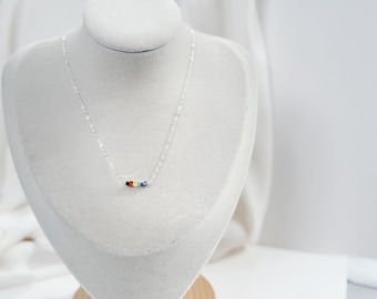 May include: A delicate silver chain necklace featuring a small, centered row of five tiny, multi-colored beads in red, orange, yellow, green, and blue. The necklace is displayed on a neutral-toned bust, highlighting the metallic links.