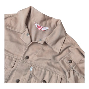 May include: Tan Levi's denim jacket with a collared neckline, button closures, and two chest pockets. The jacket features a Levi's label and buttoned cuffs. The jacket is a neutral color and has a classic design.
