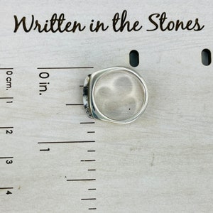 Puede incluir: Un anillo de plata con una cara cuadrada y una piedra transparente. El anillo se mide con una regla en pulgadas.