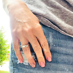 Può includere: Un anello d'argento con un design rettangolare su un dito con smalto rosa.