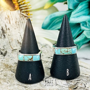 Puede incluir: Dos anillos de turquesa y plata en expositores de anillos negros. Los anillos son talla 6. El anillo de la izquierda est&aacute; etiquetado con "A" y el anillo de la derecha con "B".