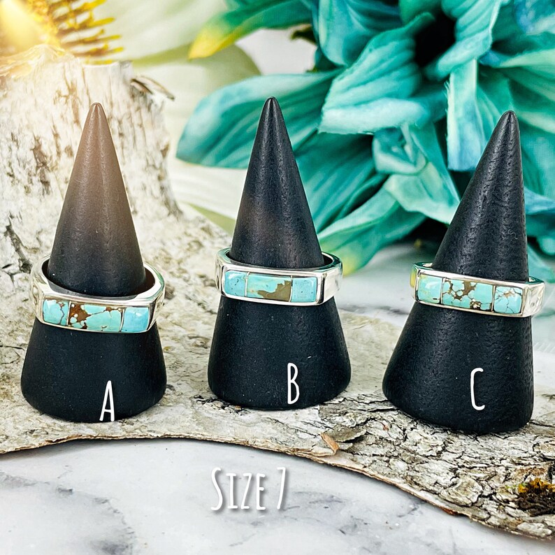 Puede incluir: Tres anillos de turquesa y plata en soportes negros. Los anillos son todos talla 7. Las piedras turquesa son de diferentes tonos de azul y verde.