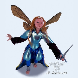May include: A handcrafted fairy figurine with wings, wearing blue armour and holding a sword. The fairy has red hair and a crown. The figurine is standing on a white background.