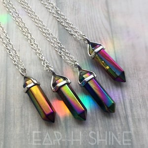 May include: Four silver necklaces with iridescent rainbow crystal point pendants. The necklaces are on a wooden surface.