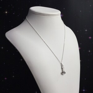 May include: A silver chain necklace with a small silver pendant shaped like a person. The pendant is detailed and has a textured surface.