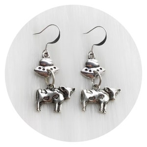 May include: Silver dangle earrings featuring a cow charm and a UFO charm.
