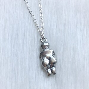 May include: Silver necklace with a pendant shaped like a woman's body. The pendant is detailed and has a smooth, shiny finish.