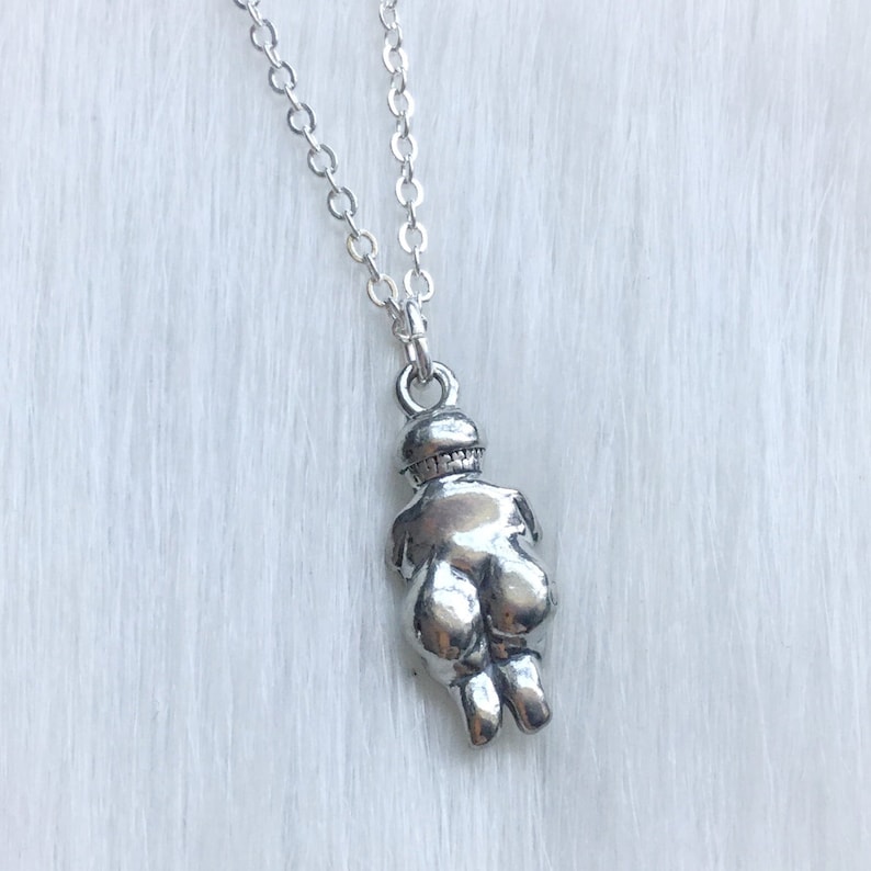 May include: Silver necklace with a pendant shaped like a woman's body. The pendant is detailed and has a smooth, shiny finish.