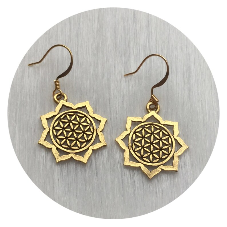 May include: A pair of gold-colored earrings. Each earring features a floral design with a geometric pattern in the center. The earrings have a hook closure.
