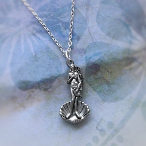 May include: A silver necklace with a pendant featuring a detailed sculpture of the Birth of Venus, a famous Renaissance artwork. The pendant depicts the goddess Venus standing on a seashell.