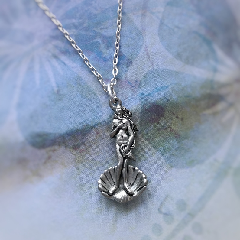 May include: A silver necklace with a pendant featuring a detailed sculpture of the Birth of Venus, a famous Renaissance artwork. The pendant depicts the goddess Venus standing on a seashell.