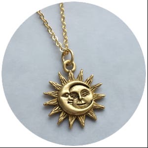 May include: Gold necklace with a sun and moon pendant. The pendant features a detailed design of a sun with a crescent moon face.