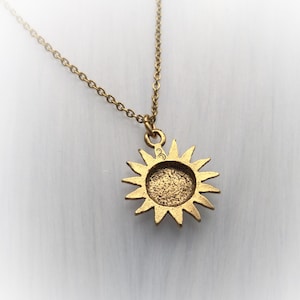 May include: Gold necklace with a sun pendant. The pendant is a detailed sun with a textured surface. The chain is a delicate, linked chain.