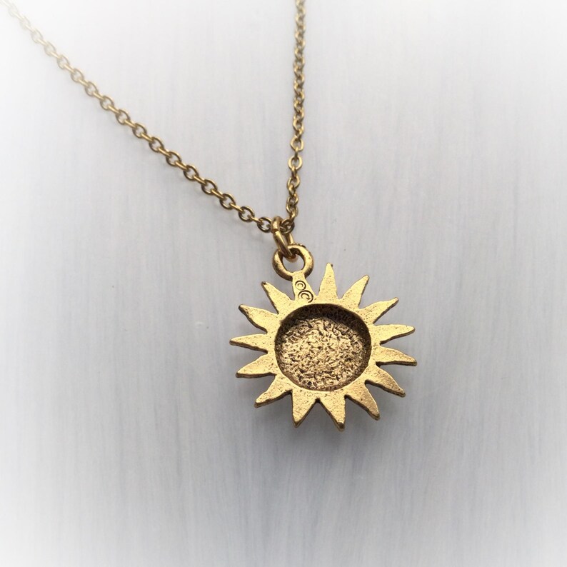 May include: Gold necklace with a sun pendant. The pendant is a detailed sun with a textured surface. The chain is a delicate, linked chain.