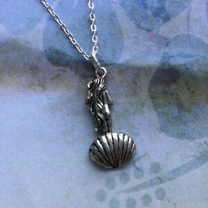 May include: A silver necklace with a pendant featuring a woman standing on a seashell. The pendant is detailed and has a vintage look.
