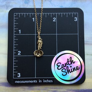 May include: Gold necklace with a bronze pendant depicting the Birth of Venus sculpture. The pendant is about 1 inch tall and the necklace is about 18 inches long. The necklace is on a black background with a ruler and a sticker that says "Earth Shine".