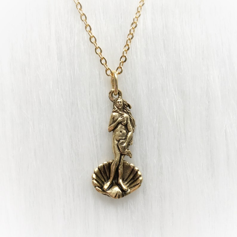 May include: A gold necklace with a pendant featuring a depiction of the Birth of Venus, a famous Renaissance sculpture. The pendant is a detailed representation of the goddess Venus standing on a seashell.