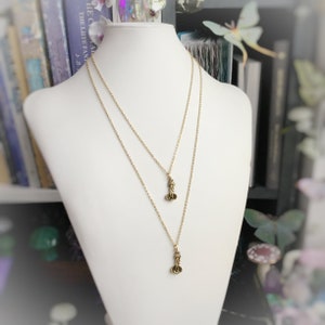 May include: A gold chain necklace with two small, delicate charms. The charms are shaped like a flower with three petals.