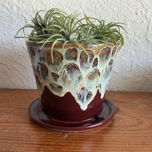 Vaso ou floreira de cerâmica moldado à mão e pintado no torno. Tons terrosos: marrom, bege, azul e vermelho. Com sistema de drenagem e pires.