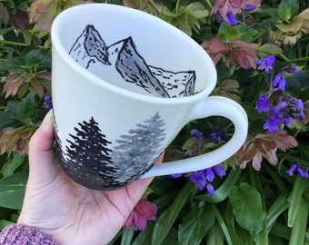 Wheel thrown and hand painted ceramic pottery mug or cup for tea or coffee. Black and white with tree design outside and mountains inside