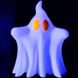 May include: A ghost-shaped lamp emitting a bright blue light with two oval-shaped orange eyes. The lamp features a smooth, flowing silhouette with a pointed top and draped edges, creating a soft glow against a dark background.