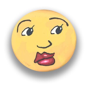 May include: A round, yellow decorative item with a painted face. The face has black eyebrows, eyes, and a small nose. The lips are red. The item is likely a decorative piece or a craft project.