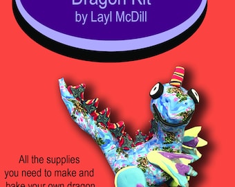 May include: A colorful dragon sculpture kit with the text "Silly Milly Dragon Kit by Layl McDill." The kit includes all supplies to make and bake a dragon sculpture. The dragon is blue, green, yellow, and purple.