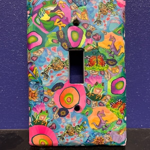 Puede incluir: Una cubierta de interruptor de luz colorida con un patrón psicodélico que presenta ranas, mariposas, flores y otros diseños caprichosos.