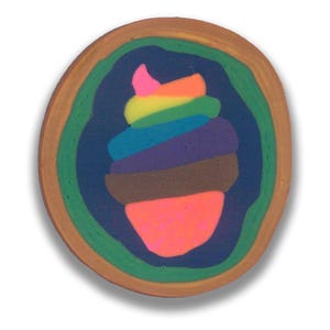 May include: A circular coaster with a layered design resembling a cupcake. The coaster has a brown outer ring, with concentric rings of green, blue, and brown surrounding a rainbow-coloured cupcake design. The cupcake has a pink top.