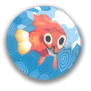 May include: A circular button with a cartoon goldfish design. The fish is orange with white details and large black eyes, set against a blue background with a swirling water pattern. The button has a white border.