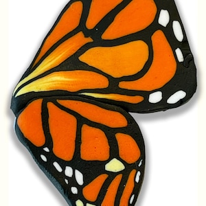 May include: A pair of monarch butterfly wings, featuring vibrant orange and black patterns with white spots. The wings are detailed with a black outline and yellow accents, creating a striking visual.