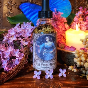 May include: A glass bottle with a dropper top and a label that reads "The Faerie Woman Enchanted Hair & Body Co.". The bottle is filled with a clear liquid and has a floral design on the label. The bottle is surrounded by purple flowers and a blue butterfly.