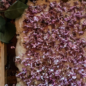 May include: A close-up of a white surface covered in small, light purple lilac blossoms.
