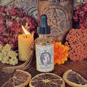 May include: A glass bottle with a dropper filled with a golden liquid. The bottle has a label that reads "Moon Goddess Magick Apothecary" and "Midsummer Sabbat Ritual Oil". The bottle is surrounded by dried flowers, a lit candle, and dried orange slices.