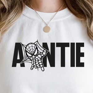 Könnte beinhalten: Weißer Pullover mit einem schwarzen Aufdruck eines Spiderman-Charakters, der hinter dem Wort "AUNTIE" hervorlugt.