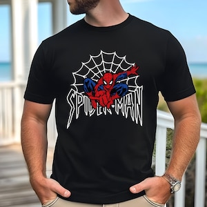 Puede incluir: Camiseta negra con un diseño de telaraña blanca y un gráfico de Spiderman rojo y azul. El texto "SPIDER-MAN" está impreso en blanco debajo del gráfico.