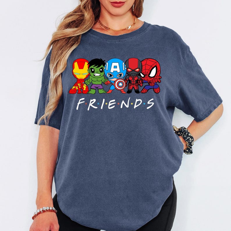 K&ouml;nnte beinhalten: Ein marineblaues T-Shirt mit einem Aufdruck von f&uuml;nf Comic-Superhelden, darunter Iron Man, Hulk, Captain America, Black Panther und Spiderman. Der Text "FRIENDS" ist unter den Superhelden gedruckt.
