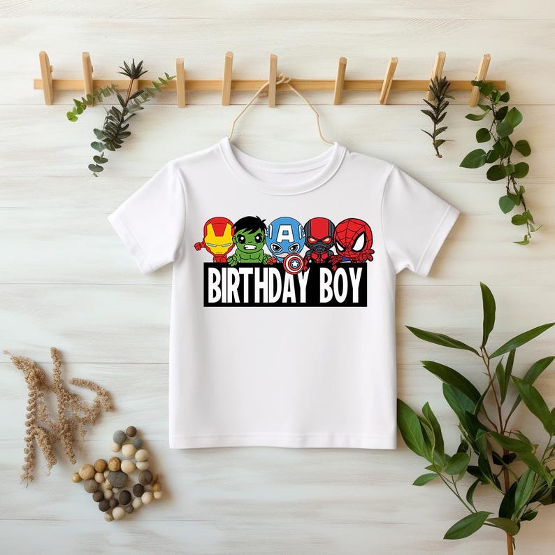 May include: White t-shirt with a graphic of five cartoon superheroes, including Iron Man, Hulk, Captain America, Black Panther, and Spiderman. The text "Birthday Boy" is printed below the graphic.