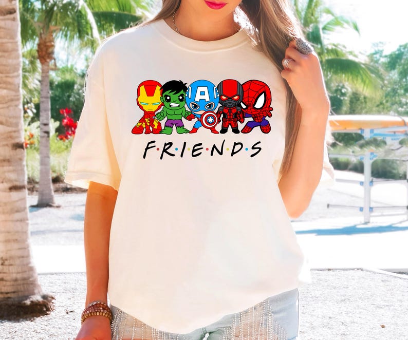 K&ouml;nnte beinhalten: Wei&szlig;es T-Shirt mit einer Grafik von f&uuml;nf Comic-Superhelden, darunter Iron Man, Hulk, Captain America, Black Panther und Spiderman. Der Text "FRIENDS" ist unter der Grafik gedruckt.