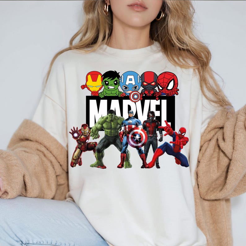 May include: White sweatshirt with a graphic print of various Marvel superheroes, including Iron Man, Hulk, Captain America, Spider-Man, and Thor. The text "MARVEL" is printed in black below the superheroes.
