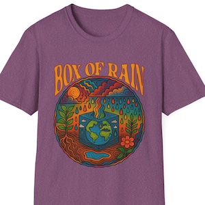 May include: Purple t-shirt with a colorful graphic design. The design features the text "BOX OF RAIN" in orange, with a circular illustration of the Earth inside a box, surrounded by plants, a flower, and rain. The shirt is made of a soft material.