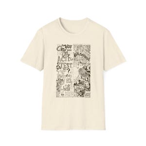 May include: Cream-colored t-shirt with a black and white graphic design. The graphic features text and illustrations, including the words "ACID TEST" and "NEAL CASADY". The shirt has short sleeves and a crew neck.