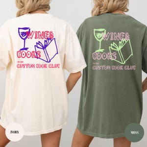 Op de afbeelding: Een ivoorkleurig en een mosgroen t-shirt, beide met een afbeelding op de achterkant van een wijnglas, een open boek en de tekst WINE & BOOKS, EST 2025, CUSTOM BOOK CLUB. Het ivoorkleurige shirt heeft paarse en rode inkt, het mosgroene shirt heeft roze en lichtgroene inkt.