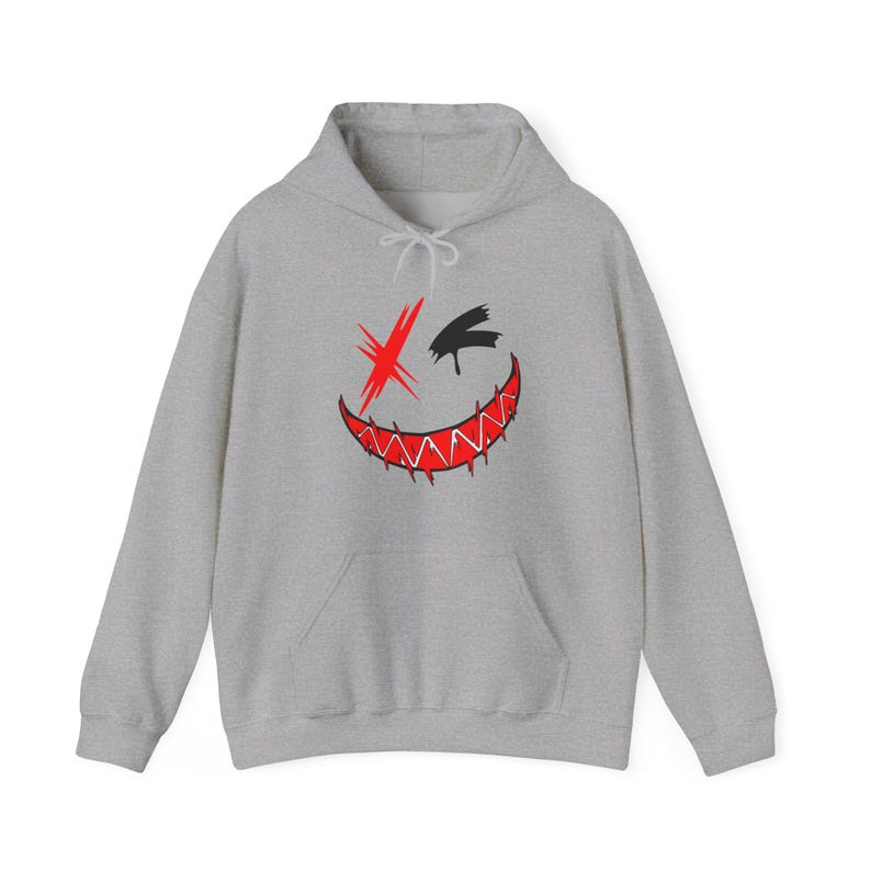 Puede incluir: Una sudadera con capucha y mangas largas en color gris jaspeado que presenta un estampado gr&aacute;fico en el pecho. El dise&ntilde;o muestra un rostro estilizado con una X roja sobre un ojo, una forma negra sobre el otro y una boca roja dentada.