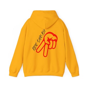 Puede incluir: Una sudadera con capucha de color amarillo brillante que presenta un gr&aacute;fico rojo de una mano haciendo el signo de la paz en la parte posterior. El texto RIDE SAFE-ISH est&aacute; impreso en letras negras inclinadas junto al gr&aacute;fico de la mano.