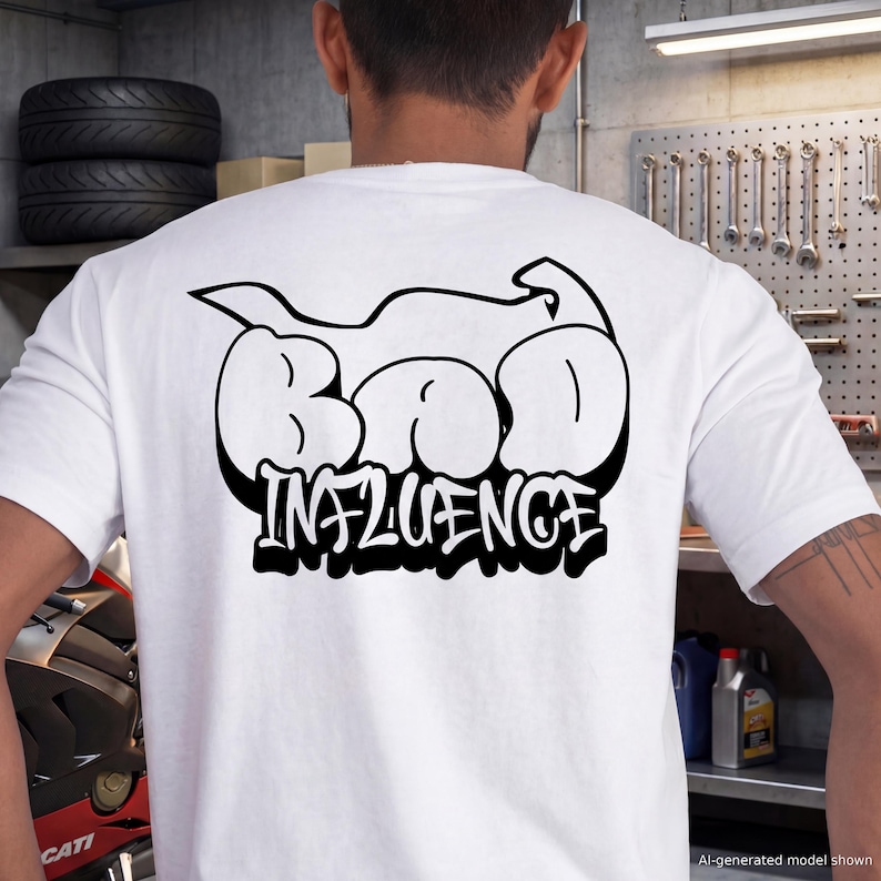 May include: A white short-sleeved t-shirt featuring a large black graphic on the back. The design displays the text "BAD INFLUENCE" in a bold, bubble-style graffiti font, positioned beneath a stylized black outline of a motorcycle silhouette.