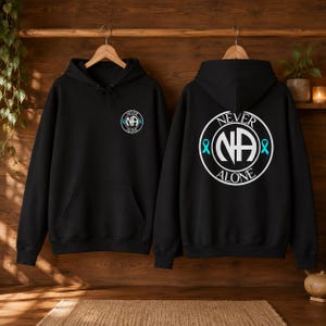 May include: A black hooded sweatshirt featuring a white circular logo on the front left chest and a larger version of the same logo on the back. The logo contains the letters NA, the text NEVER ALONE, and two small light blue awareness ribbons.