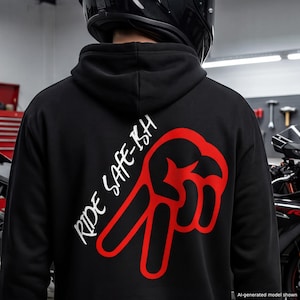 Puede incluir: Una sudadera negra con capucha que presenta un gr&aacute;fico rojo de una mano haciendo el signo de la paz en la espalda. El texto RIDE SAFE-ISH est&aacute; impreso en blanco en una fuente cursiva inclinada junto al gr&aacute;fico. La sudadera se lleva con casco.